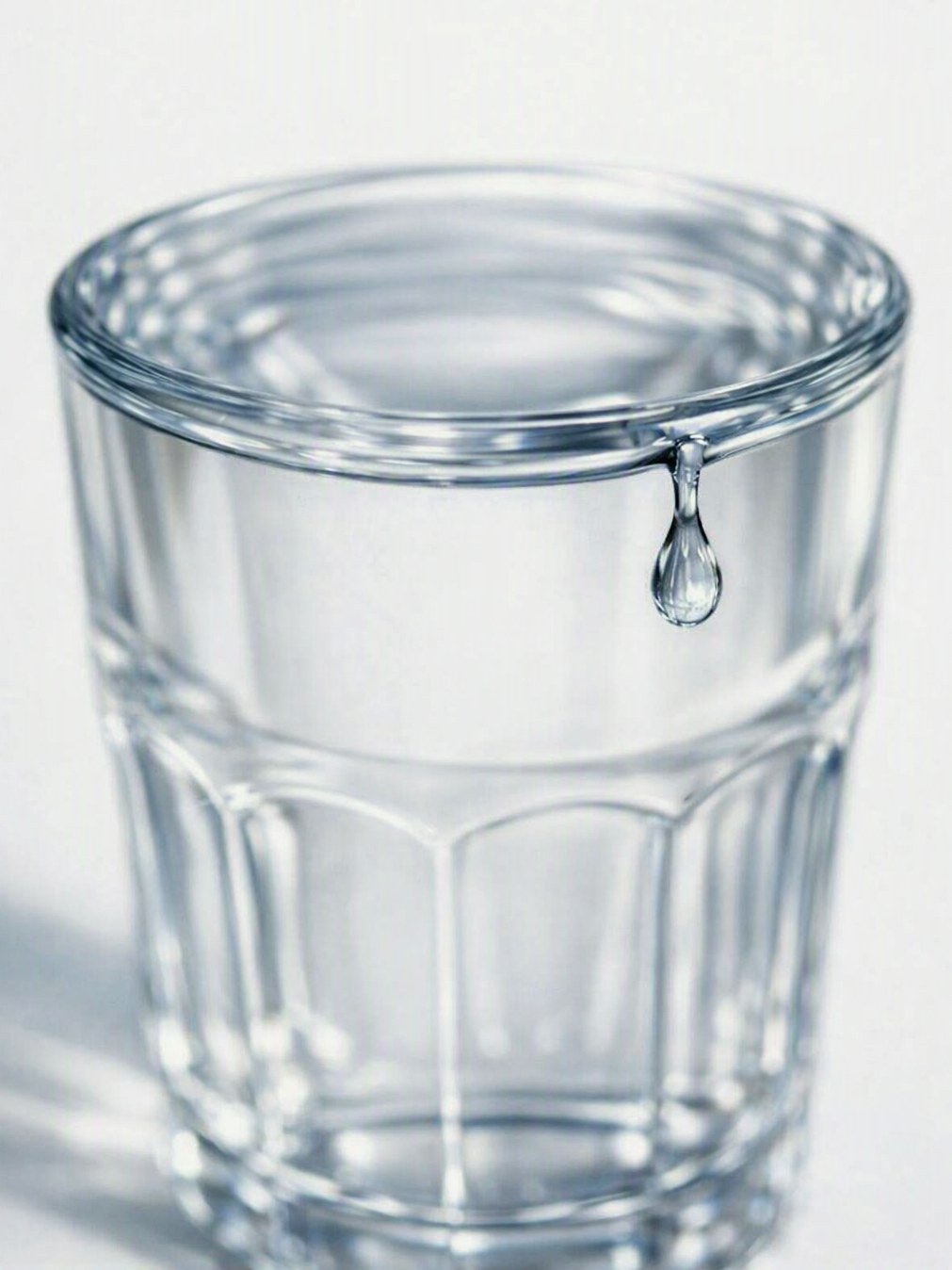 Glass of water with a single drop hanging from the rim